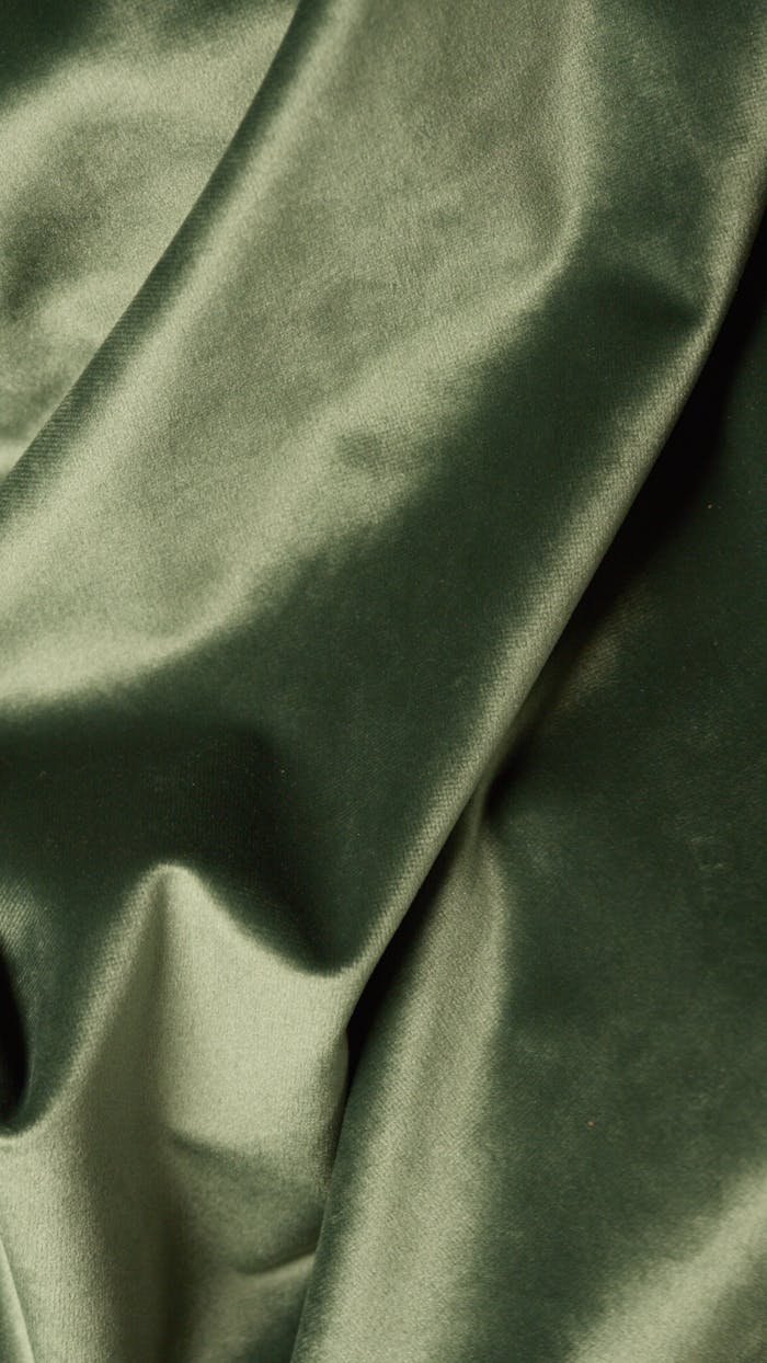 Close-up view of a smooth green silk fabric with soft shadows, perfect for textile and design themes.